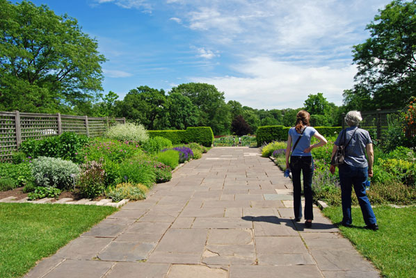 visitors walk along a stone path between perennial borders